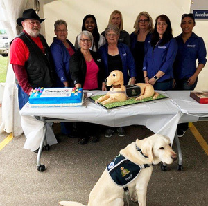 The Bonnyville Victim Services staff posed together with a large blue cake and a cake shaped like Odie, the support dog.