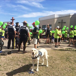 Odie the support dog standing in front of a large goup of people and police officers, green balloons scattered everywhere