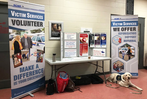 Bonnyville Victim Services table set up at an event with two large standing-banners on either side, Odie laying in front